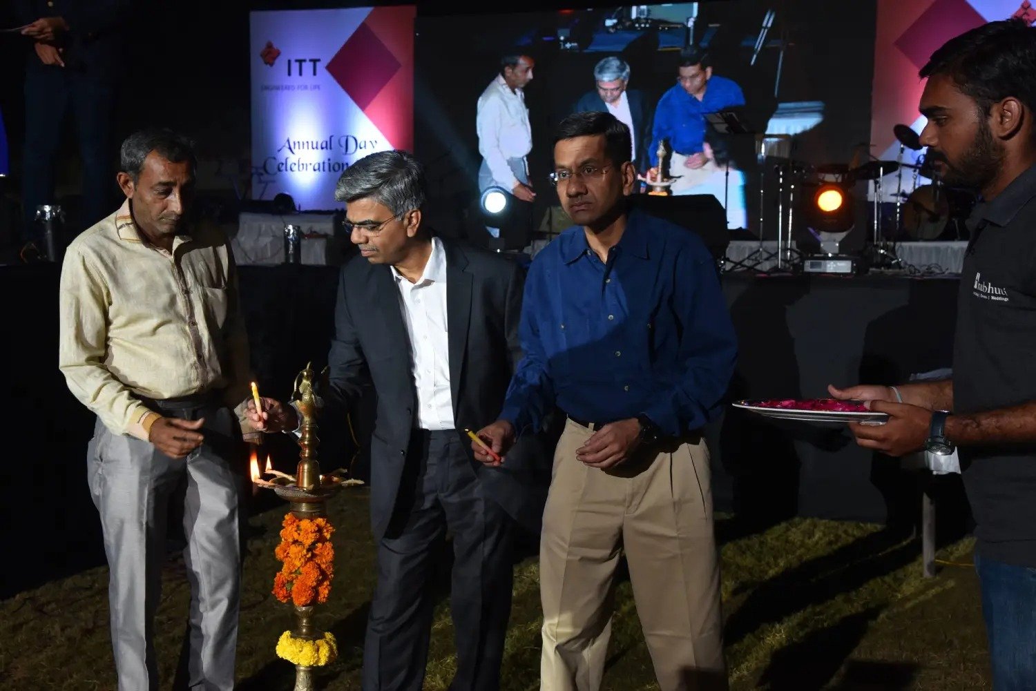 Men lighting ceremonial lamp at event with ITT banner in background